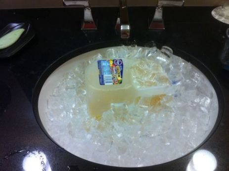 A picture of a gallon jug of orange juice in a bathroom sink full of ice.